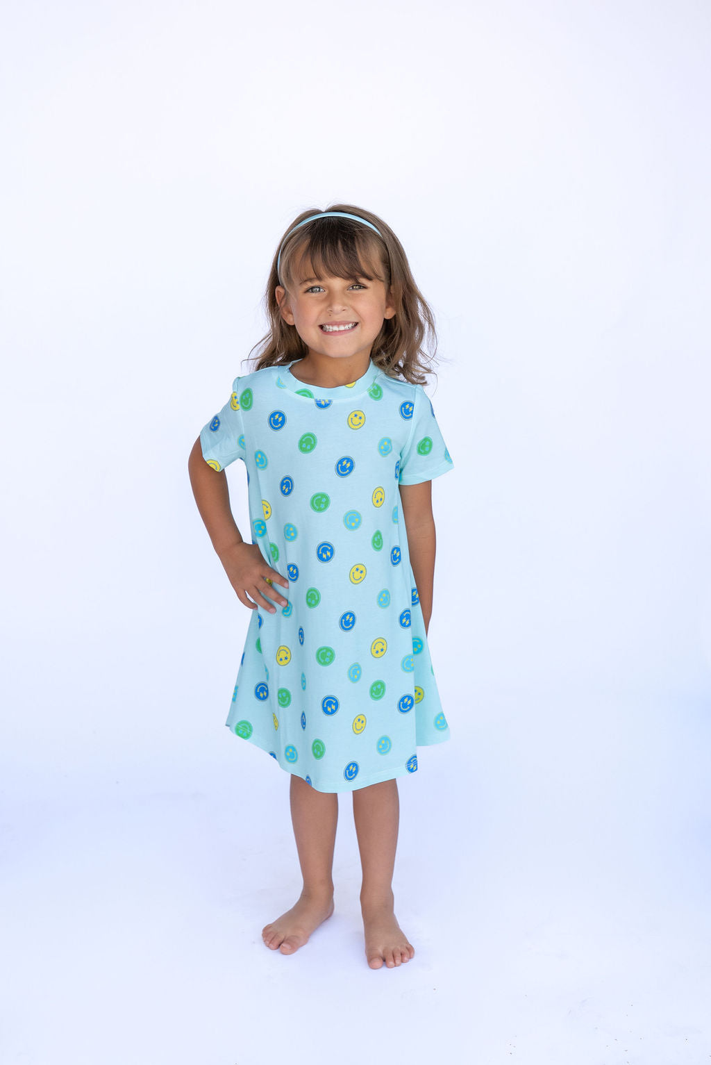 Young girl wearing a light blue dress with colorful polka dots on a white background
