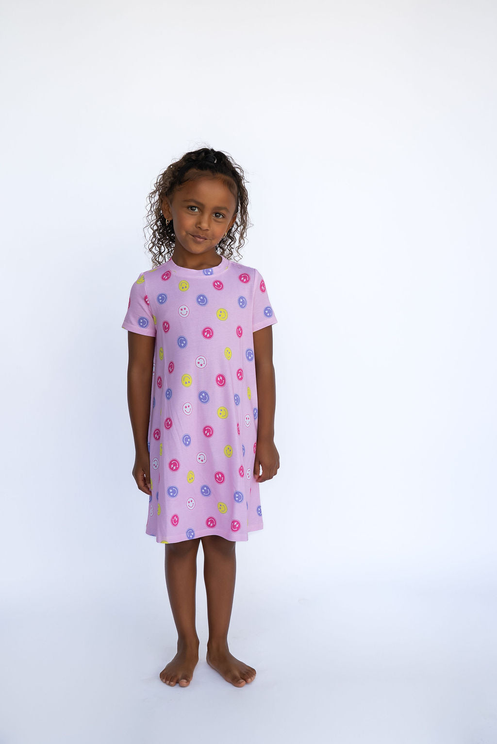 Young girl wearing a pink dress with colorful floral pattern on a white background